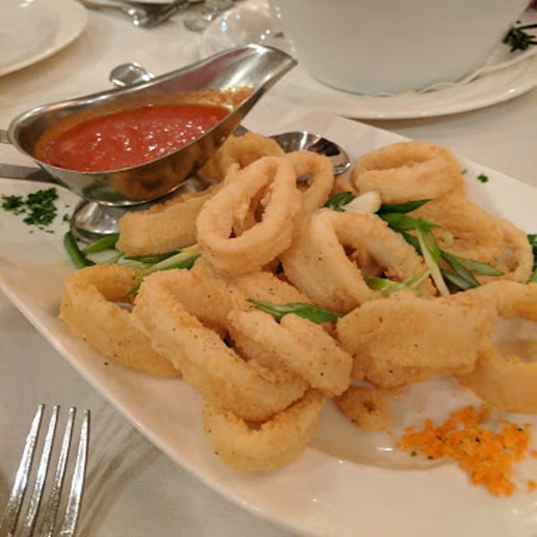 Crispy fried calamari rings with a side of red marinara sauce in a silver gravy boat.