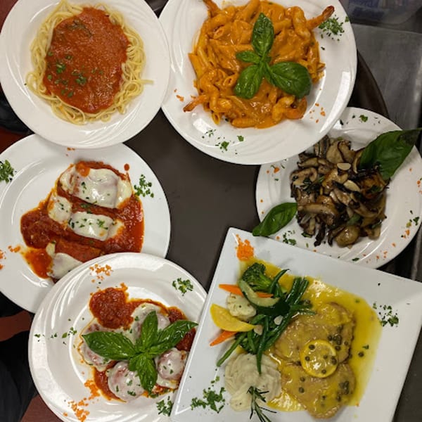 A variety of Italian dishes, including pasta, ravioli, chicken, and mushrooms, on white plates.
